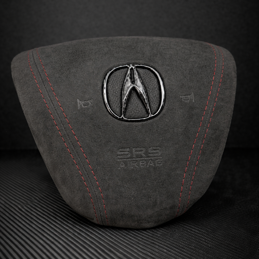 Gray airbag cover with Acura logo on a dark background